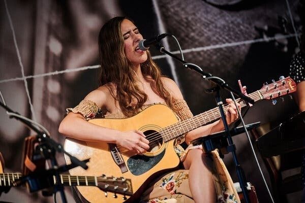 Sångerska framför mikrofon med akustisk gitarr på en scen